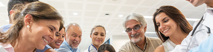 Group of healthcare workers and patients of different ages in a huddle all with hands in smiling at the hospital